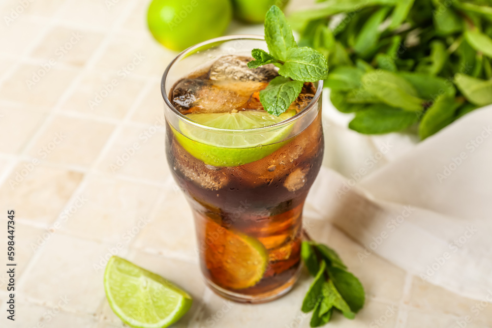 Glass of tasty Cuba Libre cocktail on light tile background