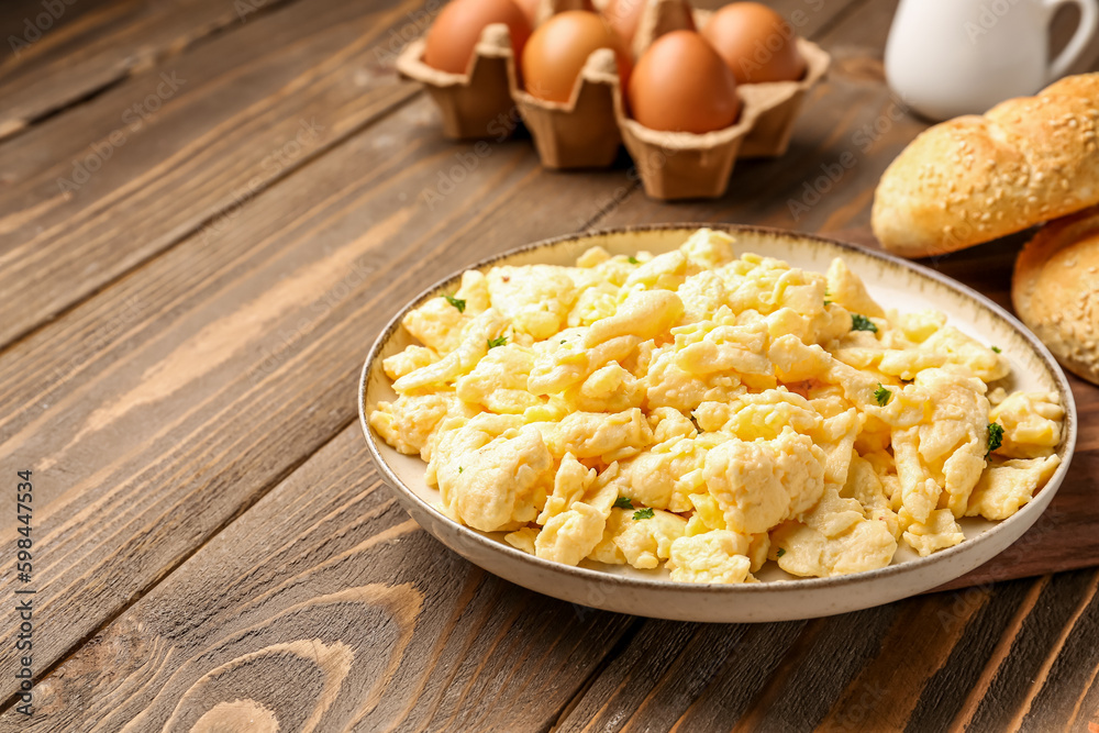 Plate of scrambled eggs and fresh buns on brown wooden background