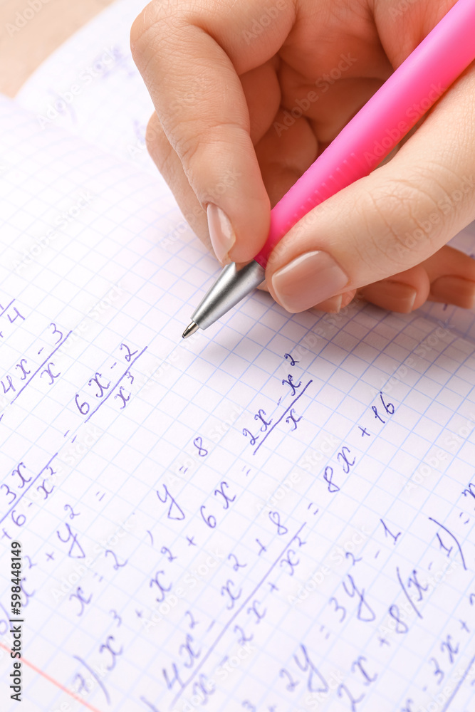 Woman writing maths formulas in copybook with pen, closeup