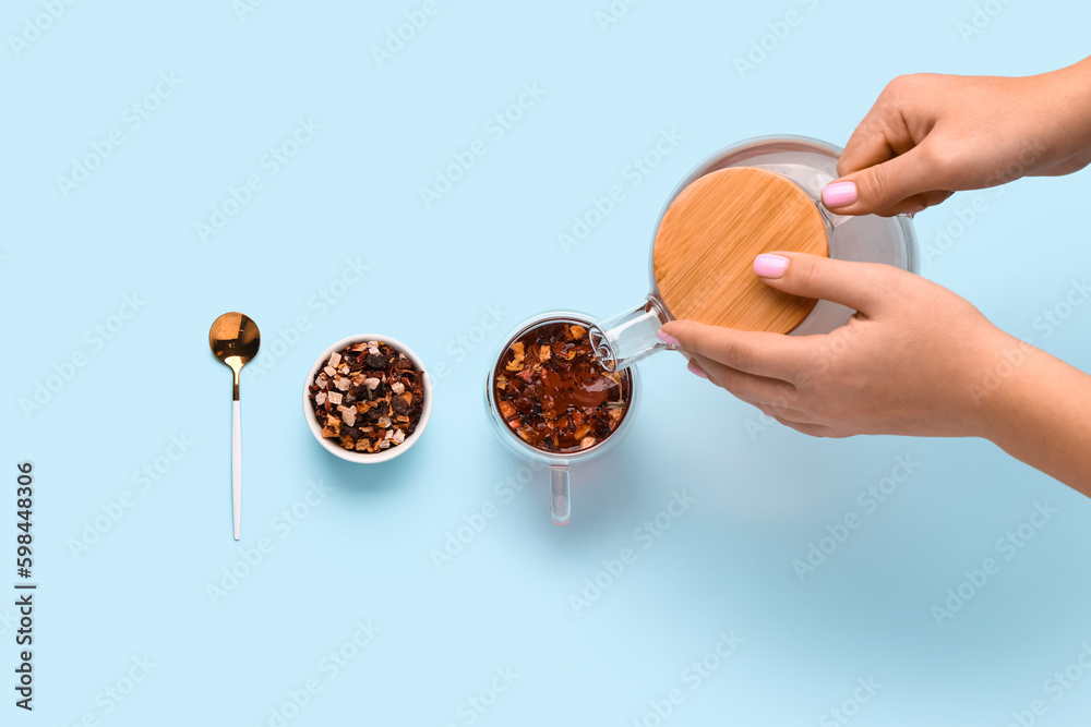 Woman pouring water from teapot into cup on blue background