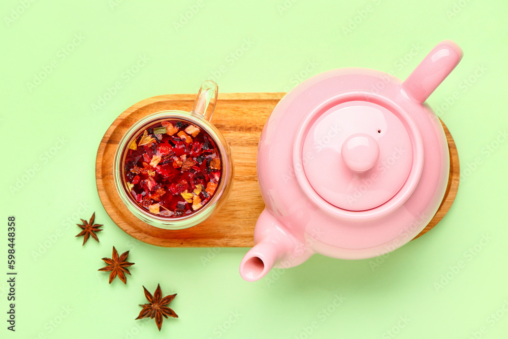 Board with teapot and cup of fruit tea on green background