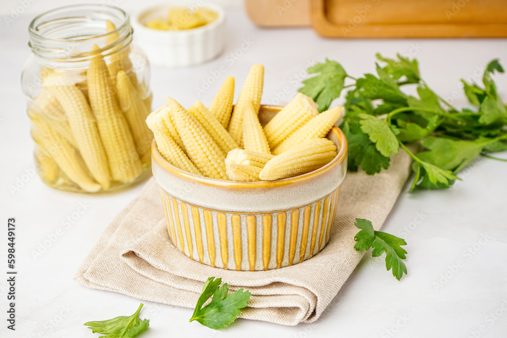 Bowl with tasty canned corn cobs on light background