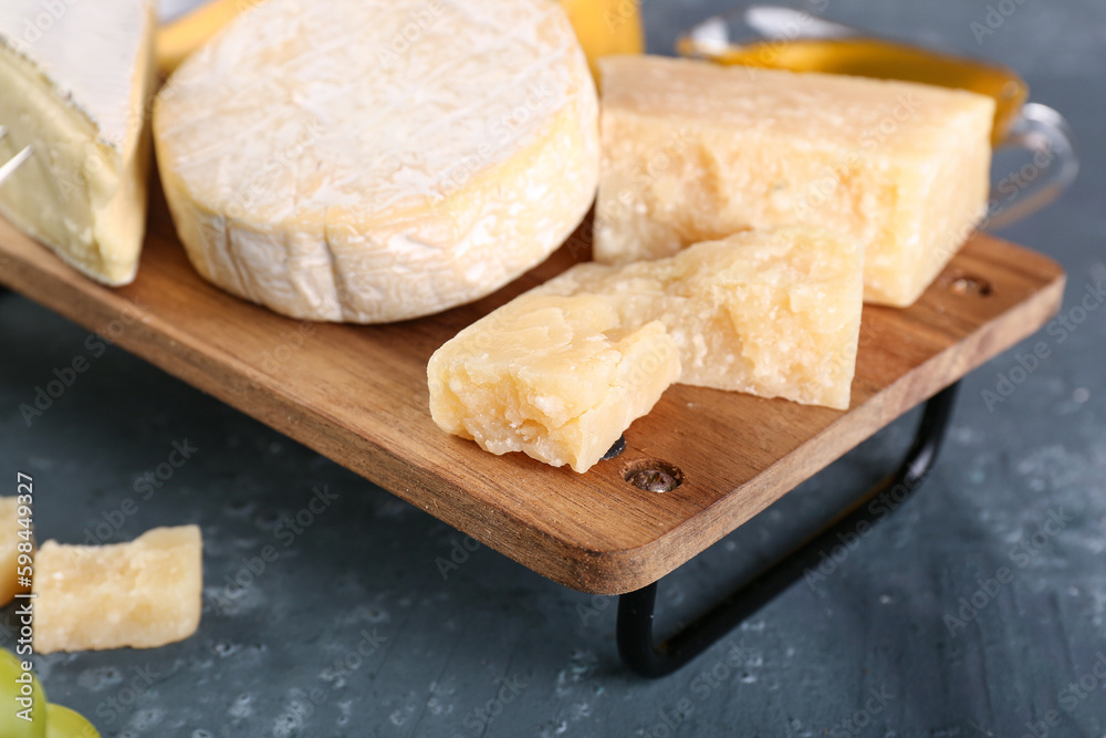 Wooden board with different types of cheese on green background, closeup