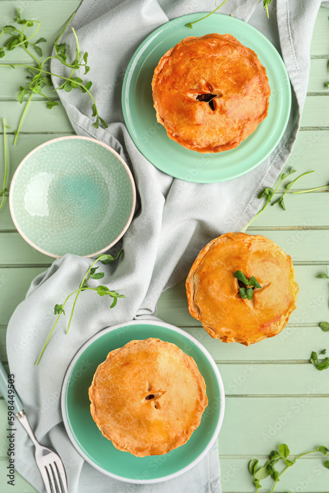 Plates with tasty meat pot pie on green wooden background