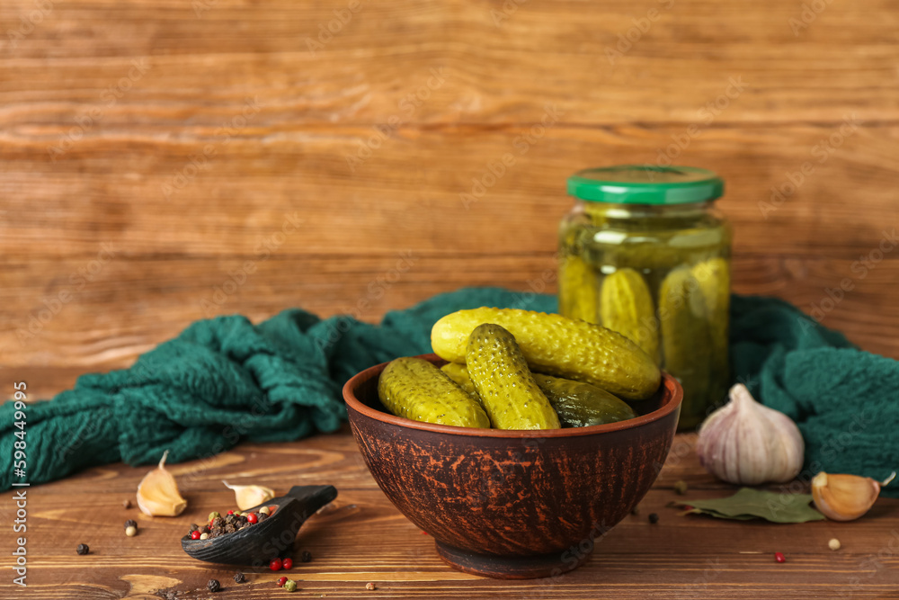 Jar and bowl with tasty canned cucumbers on wooden table