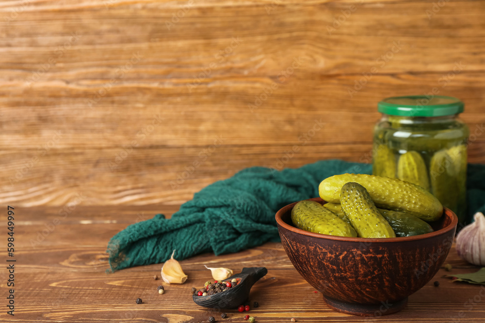 Jar and bowl with tasty canned cucumbers on wooden table