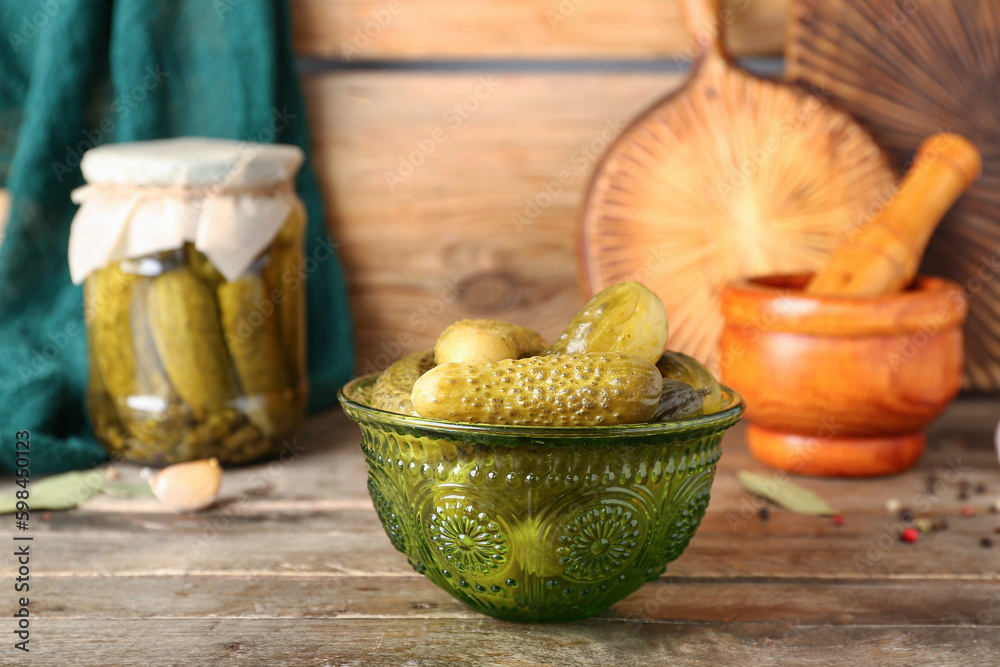 Jar and bowl with tasty canned cucumbers on wooden table