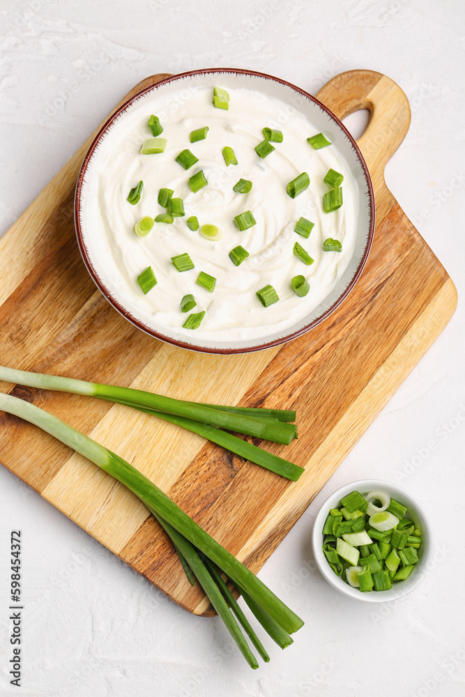 Bowl of tasty sour cream with green onion on light background