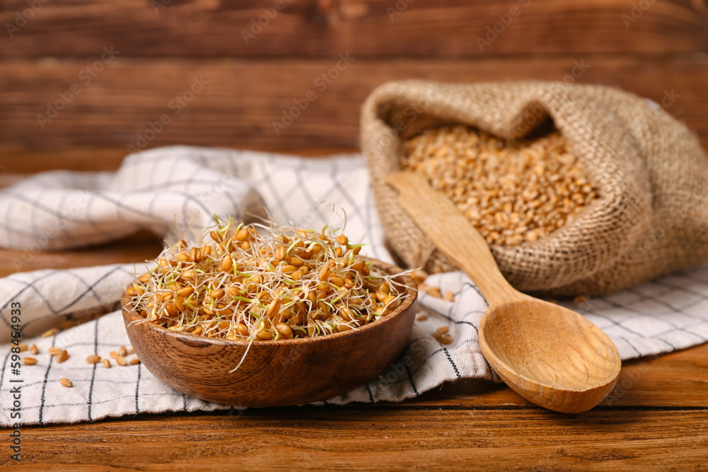 Bowl with sprouted wheat and spoon on wooden table