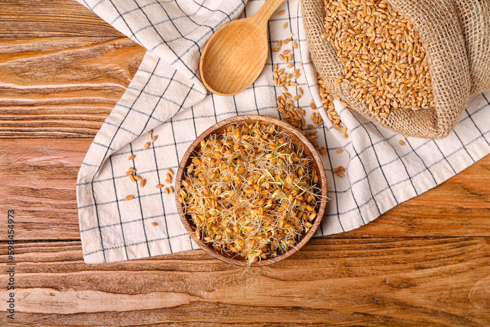 Bowl with sprouted wheat and spoon on wooden table