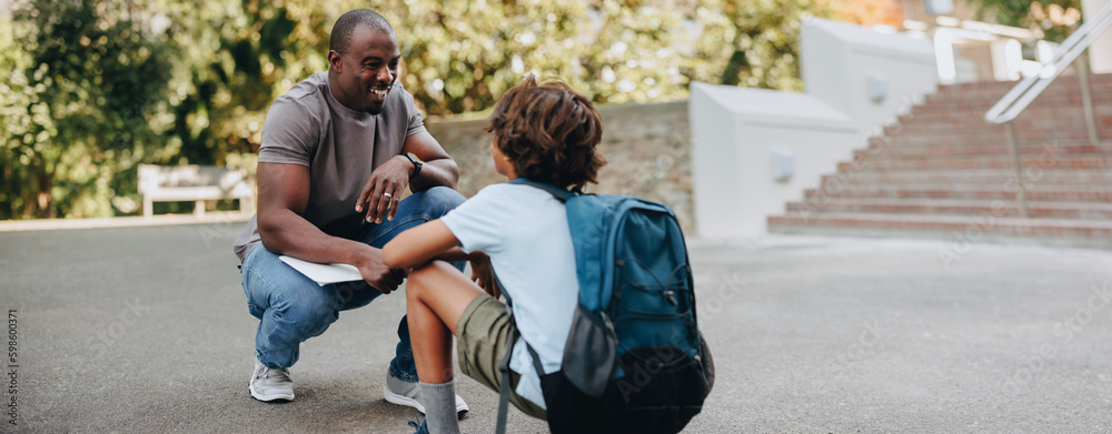 Teacher talking to a young student outdoors in a school