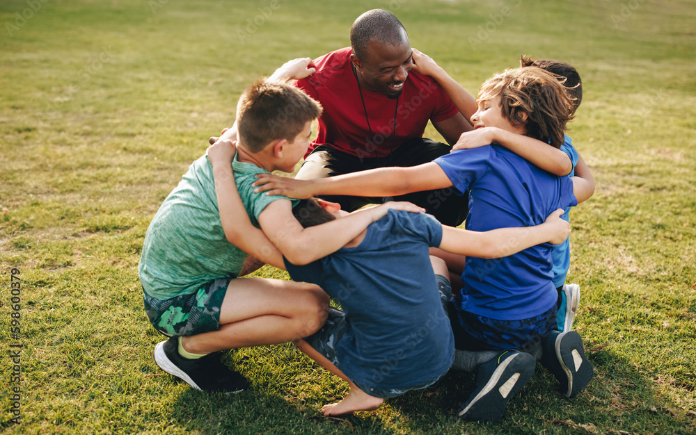 Coach and school kids huddling in a sports ground