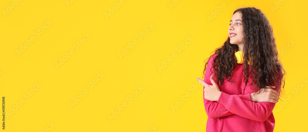 Teenage girl with headphones showing something on yellow background with space for text