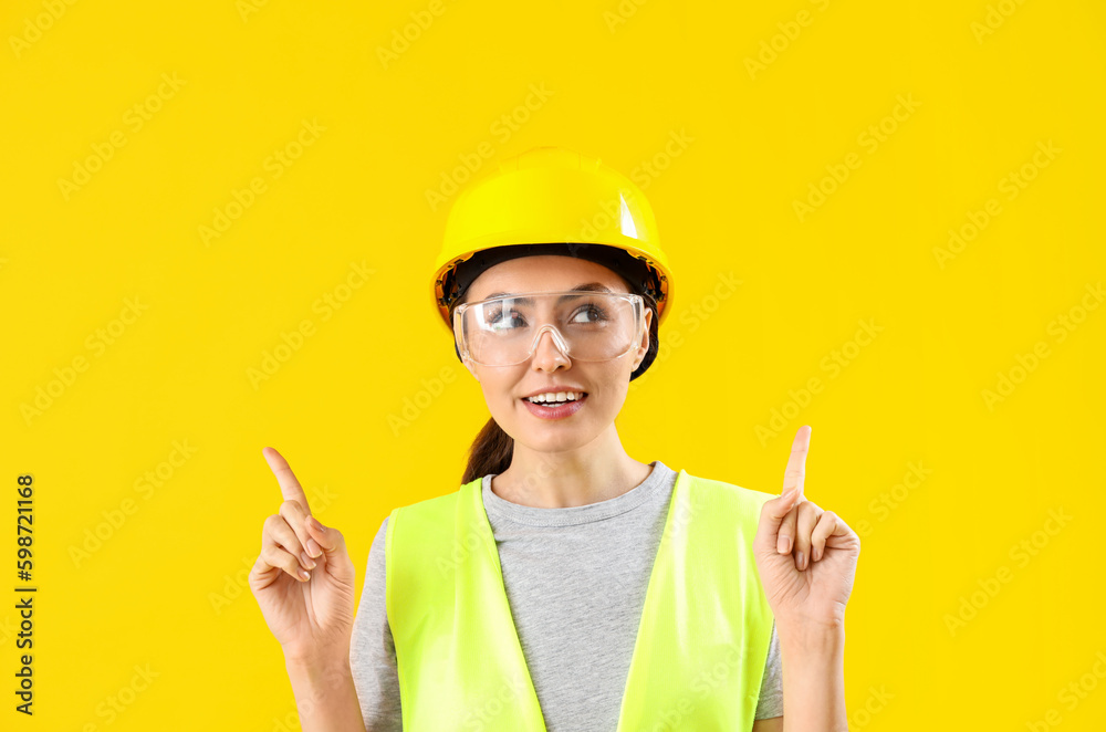 Female worker in vest pointing at something on yellow background