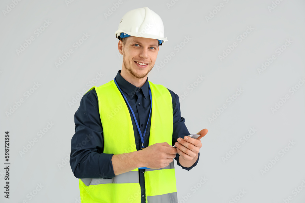 Male worker in vest and with phone on grey background