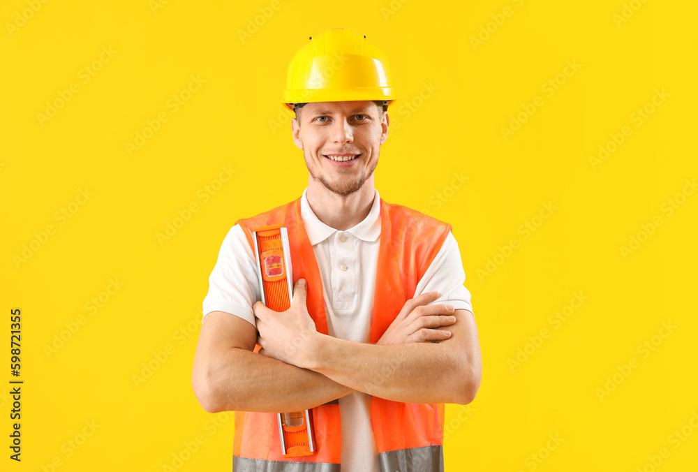 Male worker with builders level on yellow background