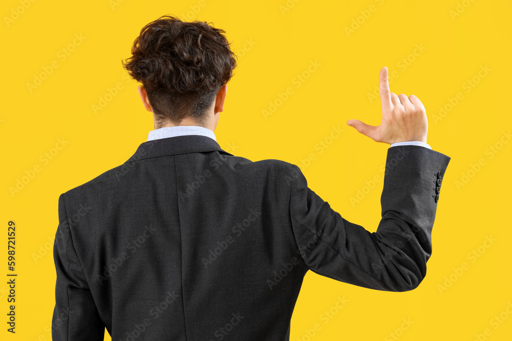 Young businessman showing loser gesture on yellow background, back view