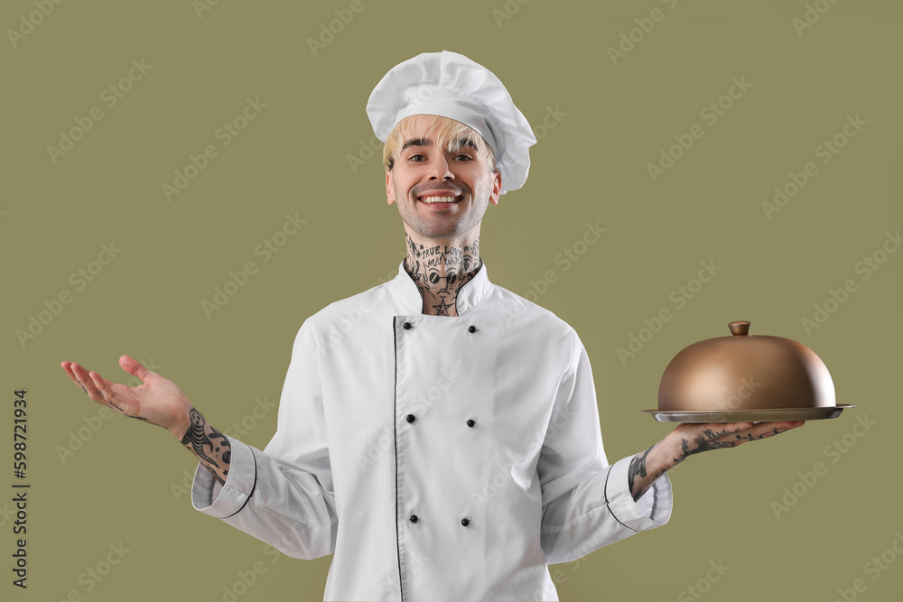 Tattooed male chef with cloche on green background