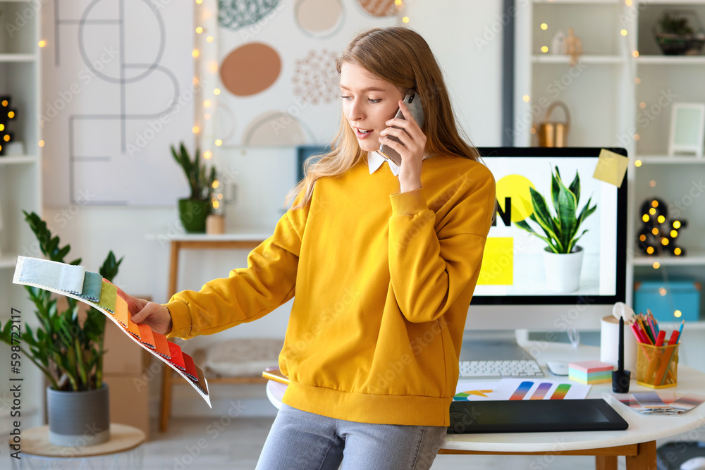 Female graphic designer with fabric samples talking by mobile phone in office