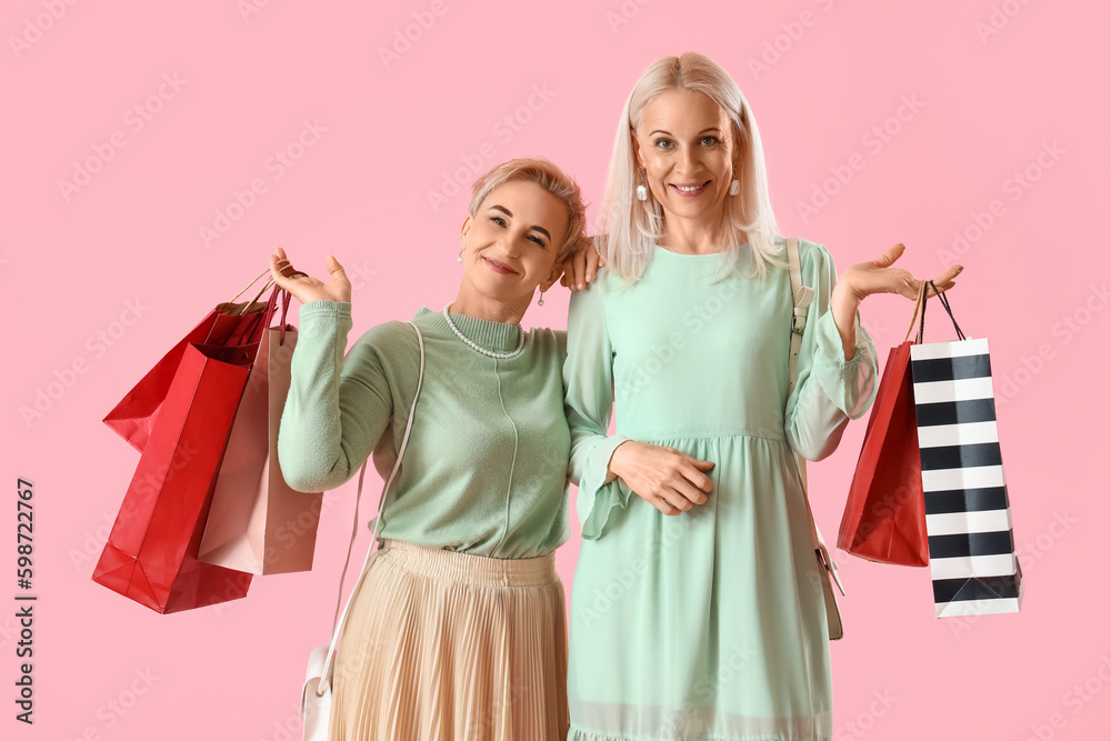 Mature women with shopping bags on pink background