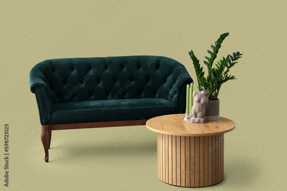 Wooden coffee table with houseplant, woman figurine and aroma candles near sofa on green background