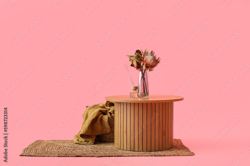 Wooden coffee table with dried flowers in vase and reed diffusers on pink background