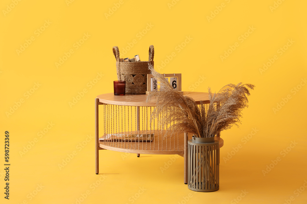 Wooden coffee table with cube calendar, wicker basket and candle holder on yellow background