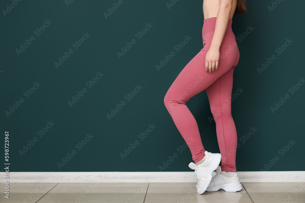 Sporty young woman in leggings near green wall