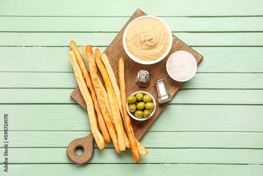 Bowl with tasty hummus and Italian Grissini on green wooden background