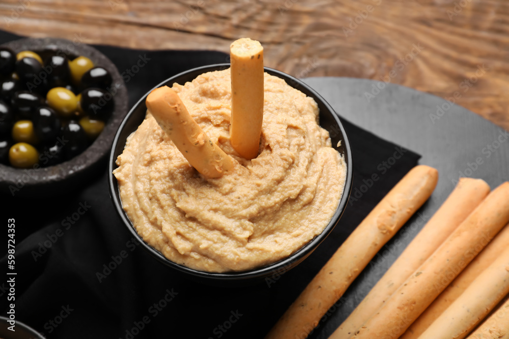 Bowl with tasty hummus and Italian Grissini on wooden background