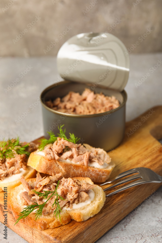 Board with delicious tuna bruschettas and tin can on grey table