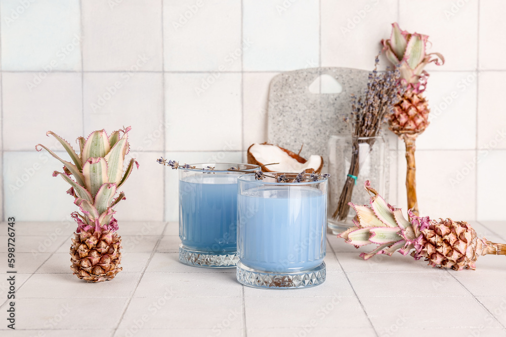 Glasses of cocktail with flowers, baby pineapples and coconut on white tile table