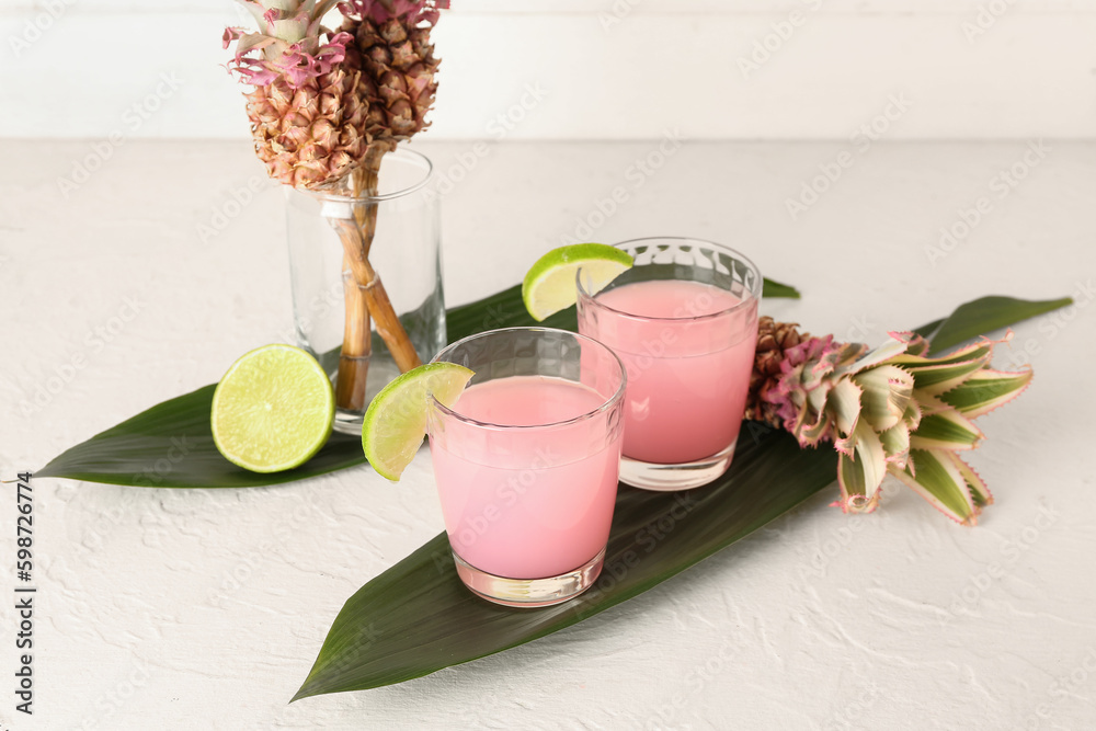 Glasses of cocktail with lime, baby pineapples and palm leaves on white table