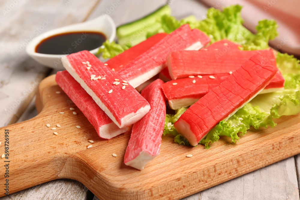 Board with tasty crab sticks on light wooden background