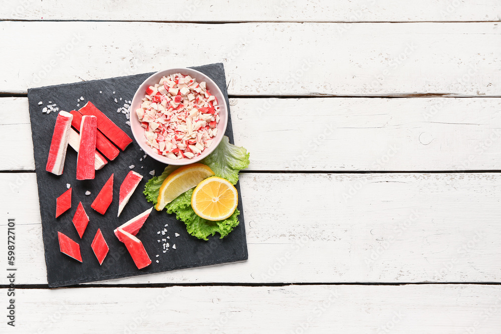 Slate board with tasty crab sticks on light wooden background