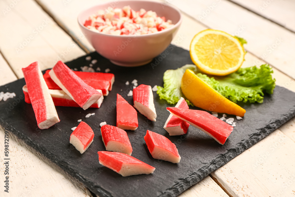 Slate board with tasty crab sticks on light wooden background