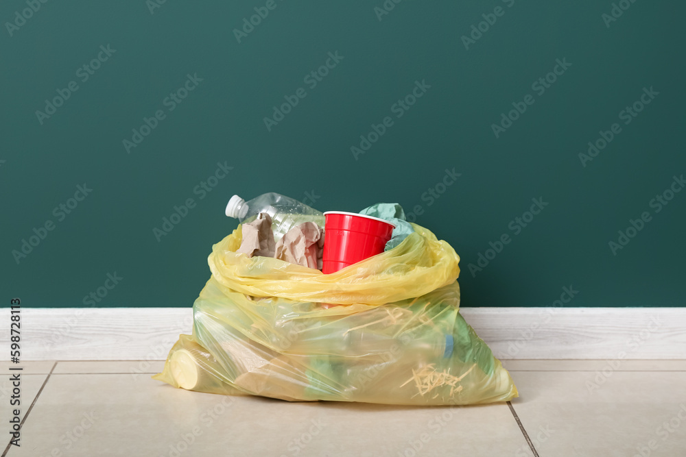 Full garbage bag near green wall