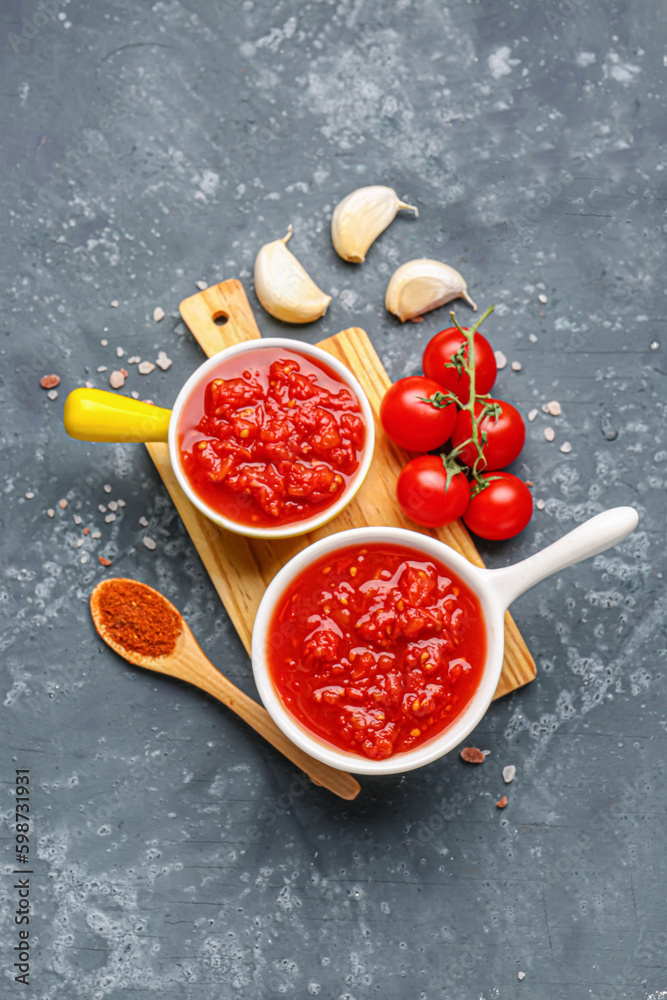 Bowls with tasty tomato sauce and fresh vegetables on blue background