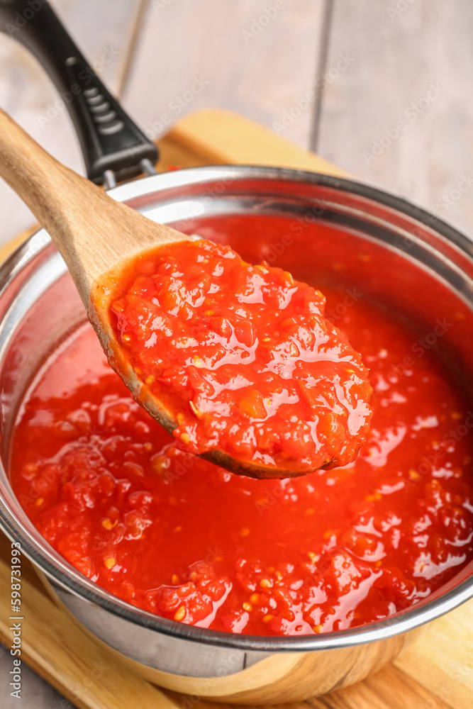 Saucepan and spoon with tasty tomato sauce on table, closeup