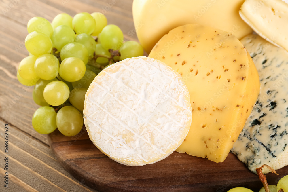 Board with different types of cheese and grapes on wooden background, closeup