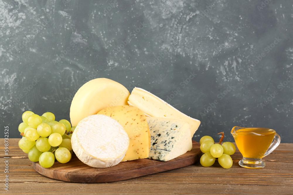 Wooden board with different types of cheese, honey and grapes on table