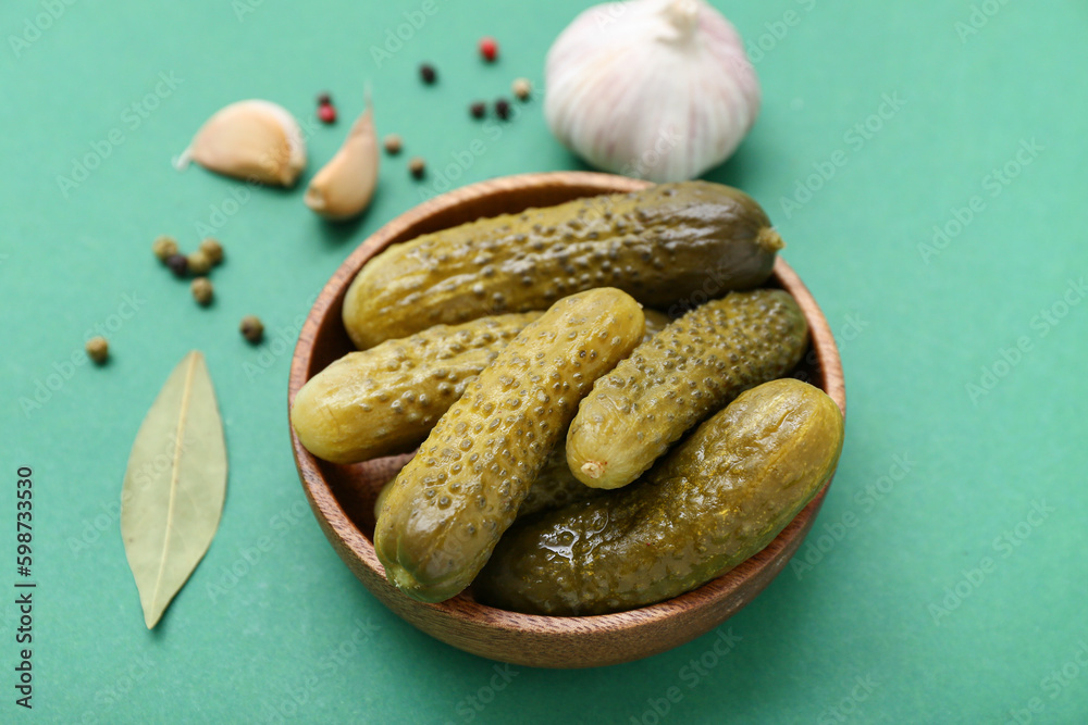 Bowl of tasty canned cucumbers with spices on green background