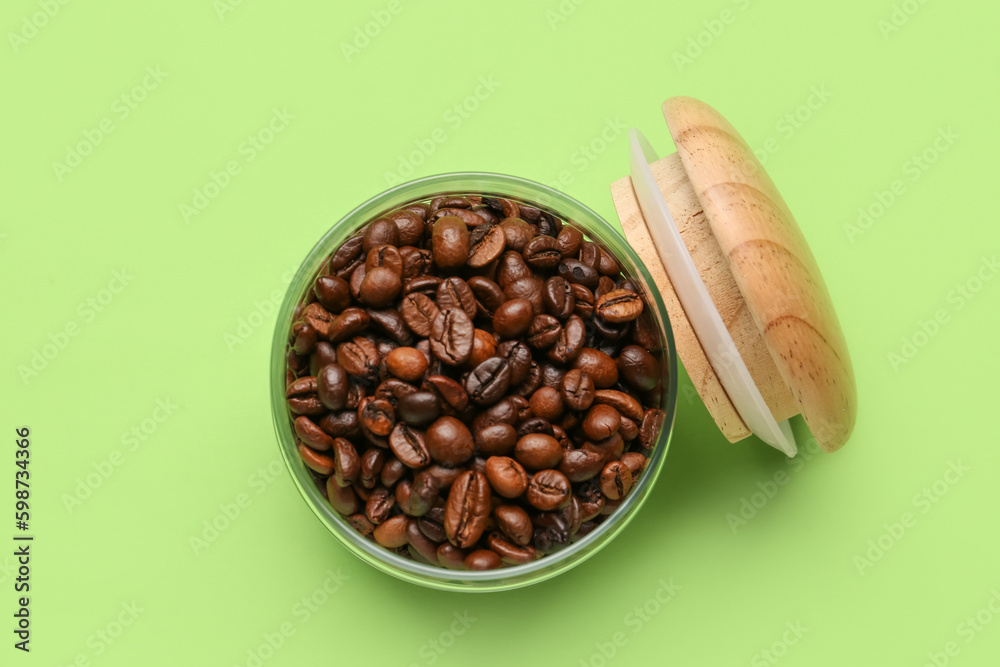 Glass jar with coffee beans on green background