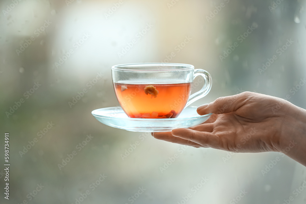 Female hand with cup of floral tea against window