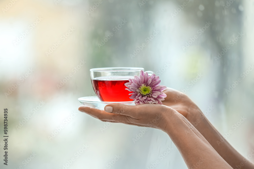 Female hand with cup of floral tea against window