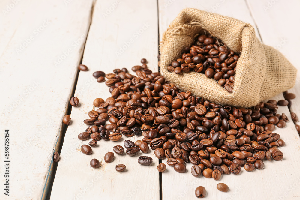 Bag with coffee beans on light wooden background