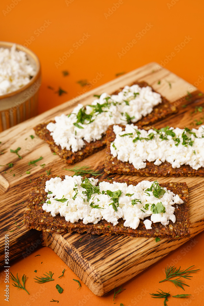 Wooden board with tasty cottage cheese and rye bread on orange background