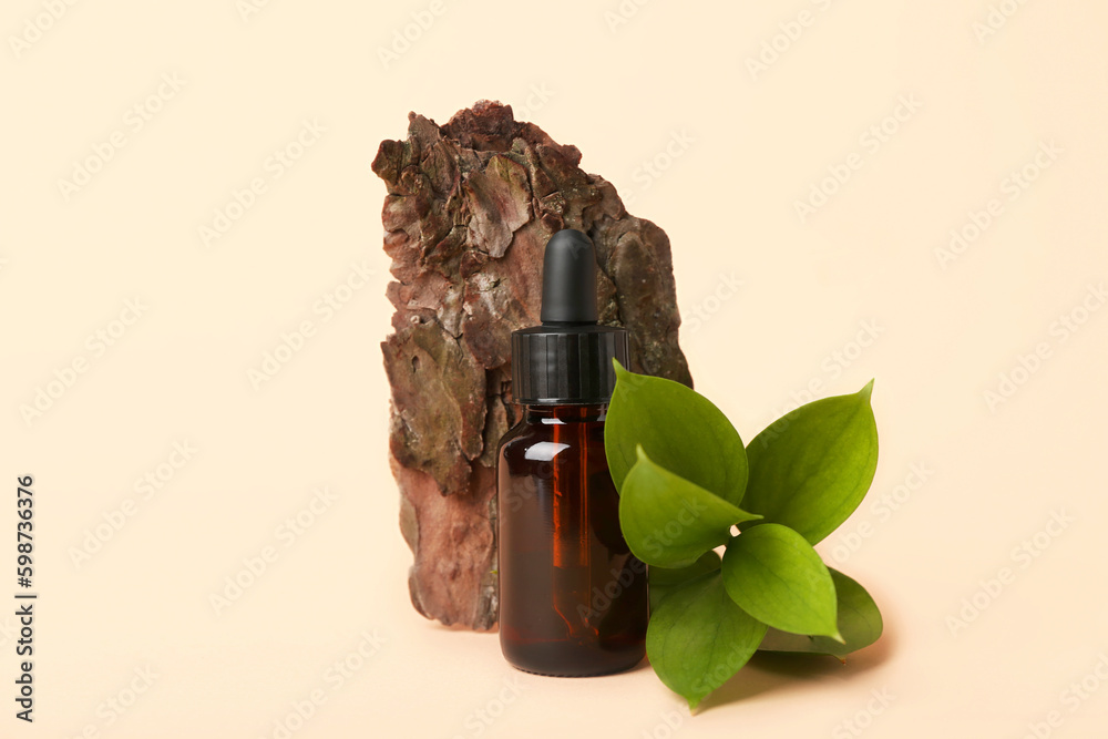 Bottle of cosmetic oil with plant twig and tree bark on beige background