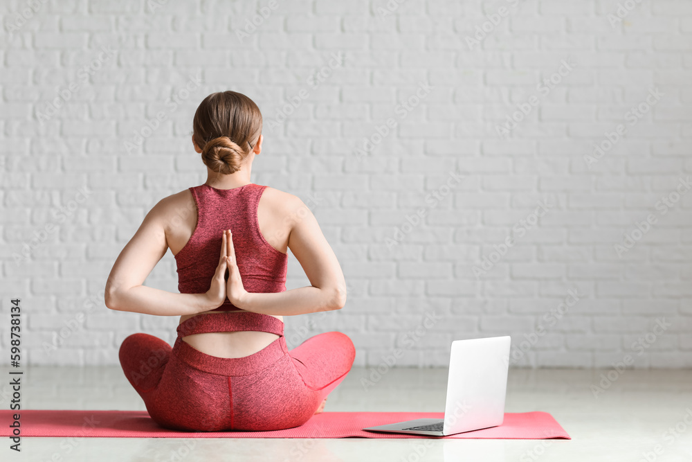 Sporty young woman with laptop doing yoga indoors