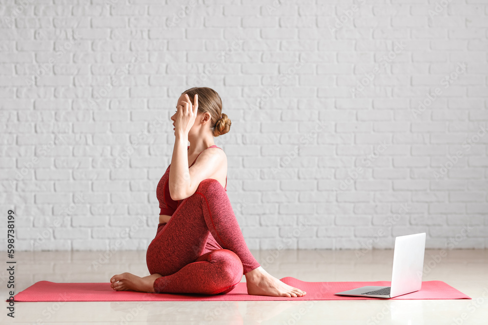 Sporty young woman with laptop doing yoga indoors